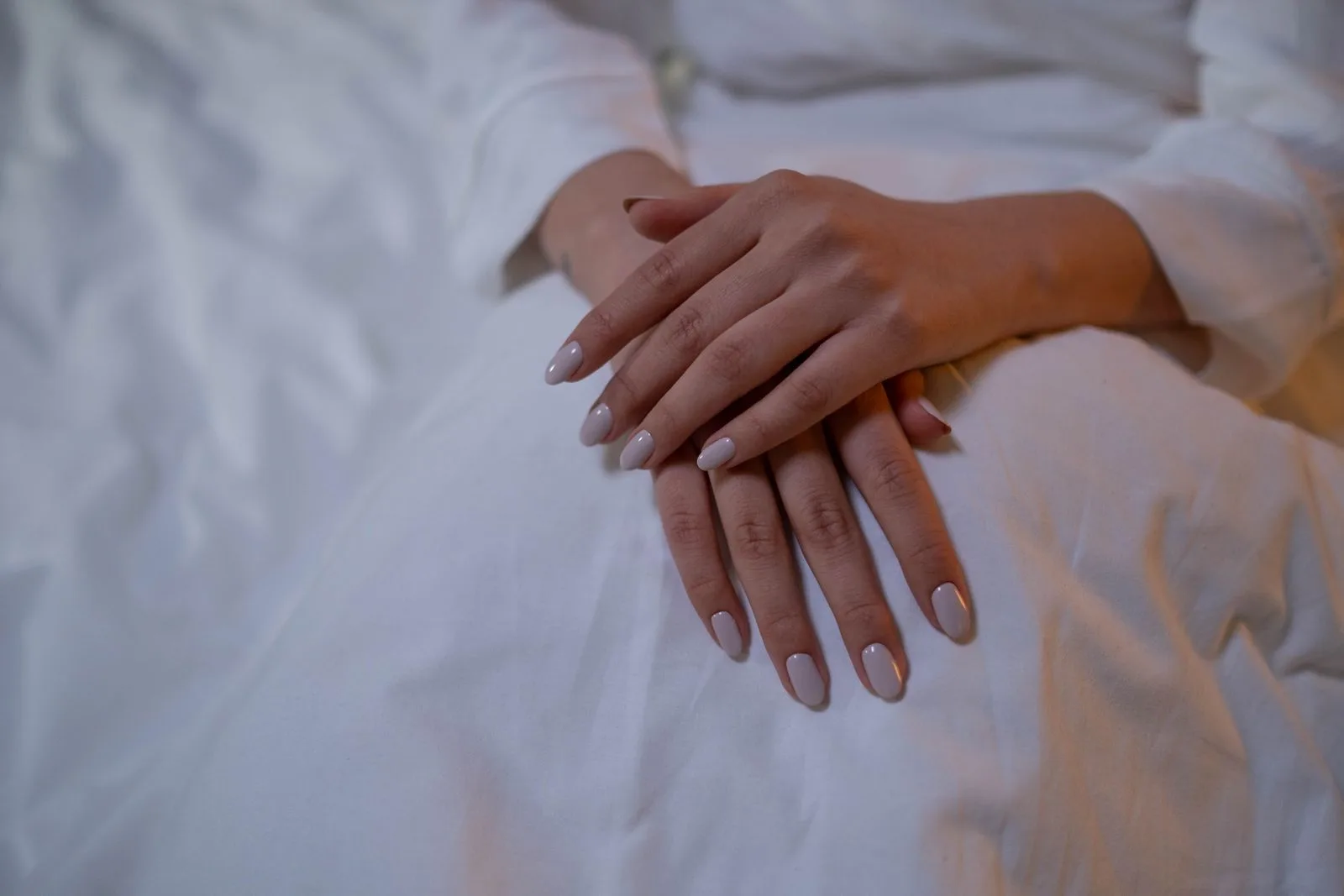 Mâini odihnite pe o pătură albă, cu unghii nude scurte
