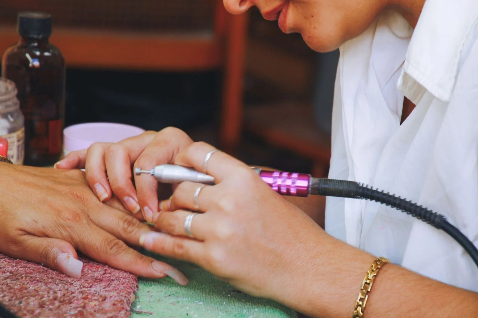 Tehniciană îndepărtând gelul cu freza, de pe unghia unei cliente